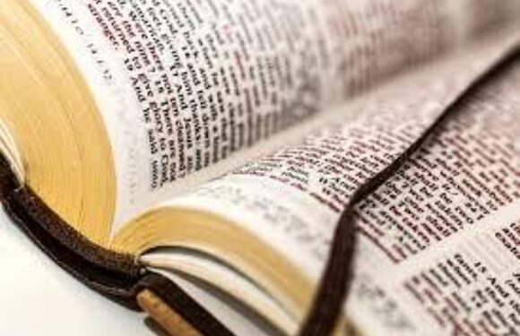 Open book with dense text pages, partially wrapped with a leather strap and lying on a light surface