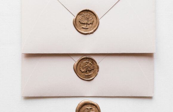 Three cream-colored envelopes stacked with gold wax seals featuring a tree design, arranged vertically, with the bottom envelope's flap open.