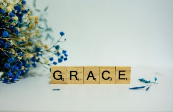 Scrabble tiles spelling out "GRACE" with blue dried flowers on the left and scattered on white surface.