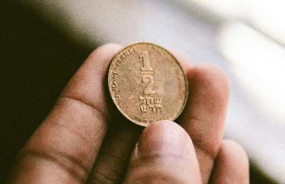 Hand holding a coin showing “1” and Hebrew text, close-up with soft blurred background.