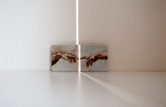 A small artwork depicts a detail of Michelangelo's "The Creation of Adam," with light and shadow creating a line of separation between two blocks on a white surface.