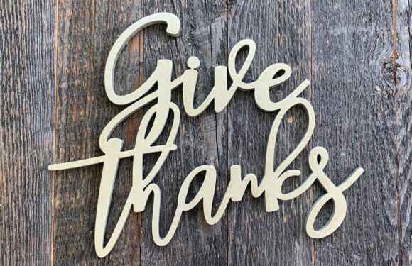 A white handwritten-style sign spelling "give thanks" is placed on a weathered wooden surface.