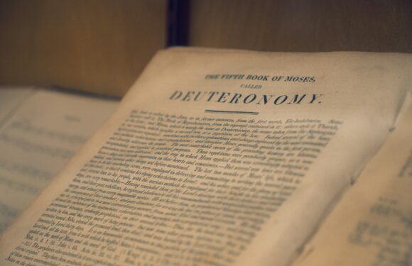 Open book on a table, close-up of the page headline “DEVUERAONOMY” with blurred text and warm lighting