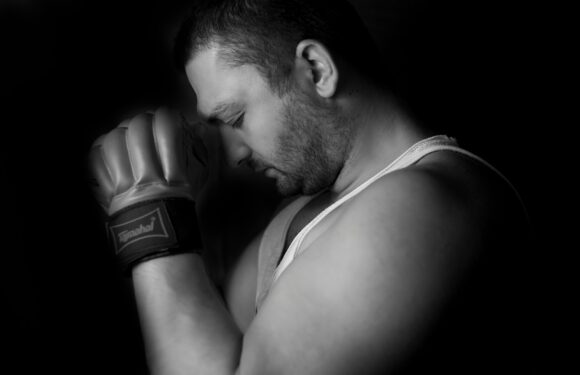 Black-and-white portrait of a person with a boxing glove, head bowed and eyes closed, softly lit against a dark background.