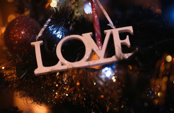 A decorated Christmas tree features a wooden "LOVE" ornament, candy canes, and gold beads, illuminated by warm and cool fairy lights.