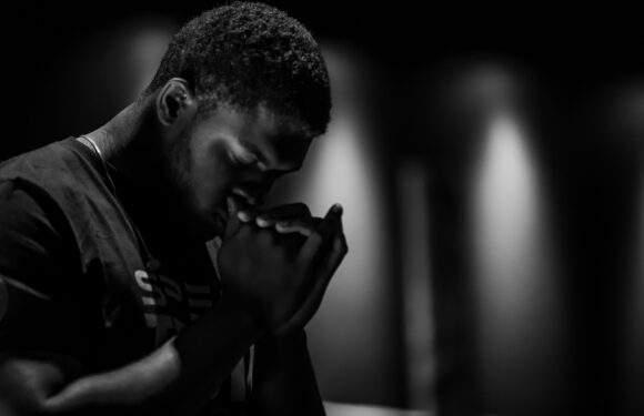 Man with head down and hands folded praying.