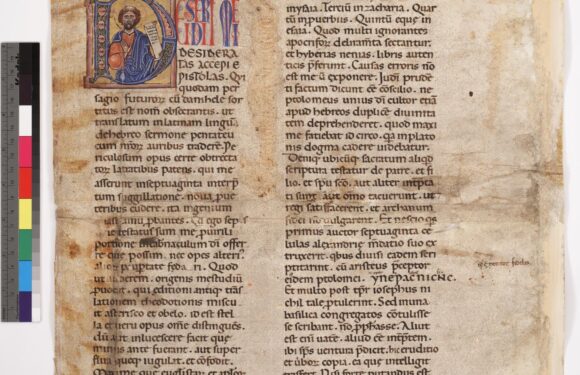A page from an ancient manuscript featuring a decorated initial of a seated figure holding a scroll, with Latin text on aged, worn parchment.