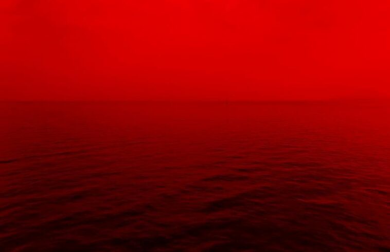 Red ocean at dusk with gentle waves and a glowing red sky stretching across the horizon.