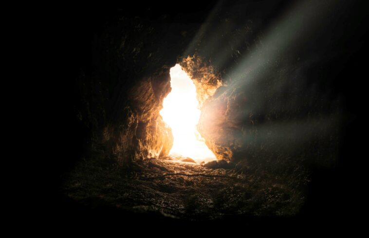 Sunlight streams into a dark cave through an opening, illuminating the rocky interior with a soft glow and creating a contrast between shadow and light.