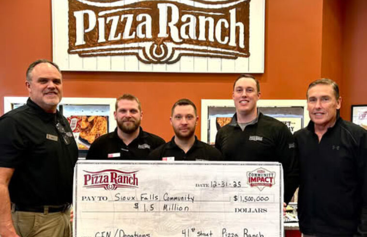 Five people in uniforms standing in front of a Pizza Ranch sign, holding an oversized check for $1.5 million made out to Sioux Falls Community.