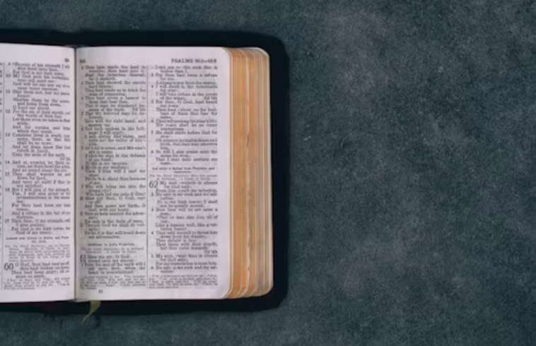 Open Bible on a dark textured surface, pages lit with margin highlights, with space to the right for text or design.