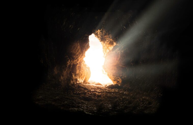 Bright sunlight shines through a cave's opening, illuminating the rough, rocky interior and creating a dramatic contrast between darkness and light.