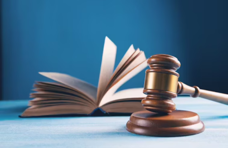 An open book on a blue surface with a wooden gavel resting beside it, against a blue background.