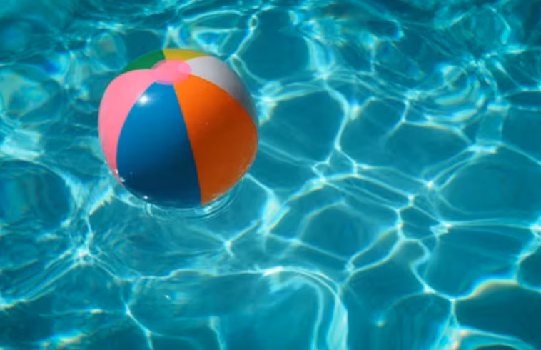 Colorful beach ball floating on rippling turquoise water with sunlight reflections.