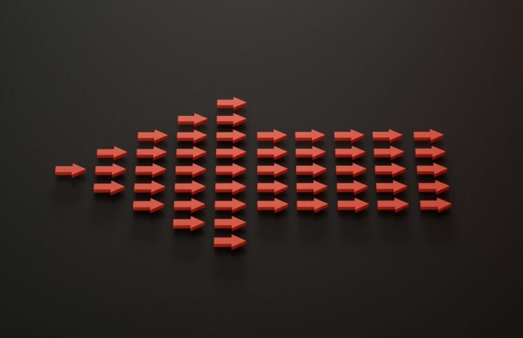 Red 3D arrows arranged like a wave, forming a long burst shape over a dark gray background, pointing rightward.