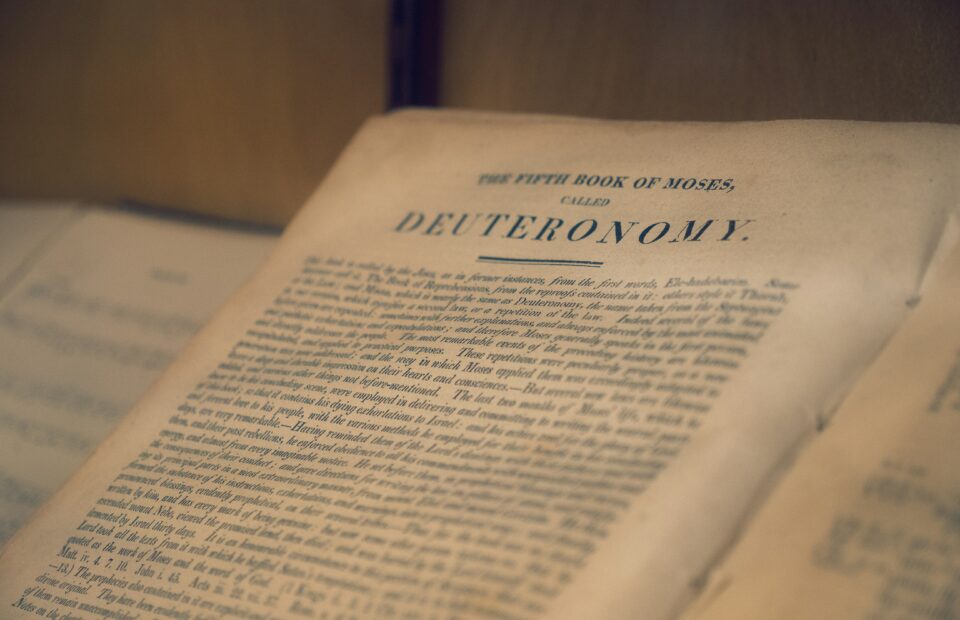 Open book on a table, close-up of the page headline “DEVUERAONOMY” with blurred text and warm lighting