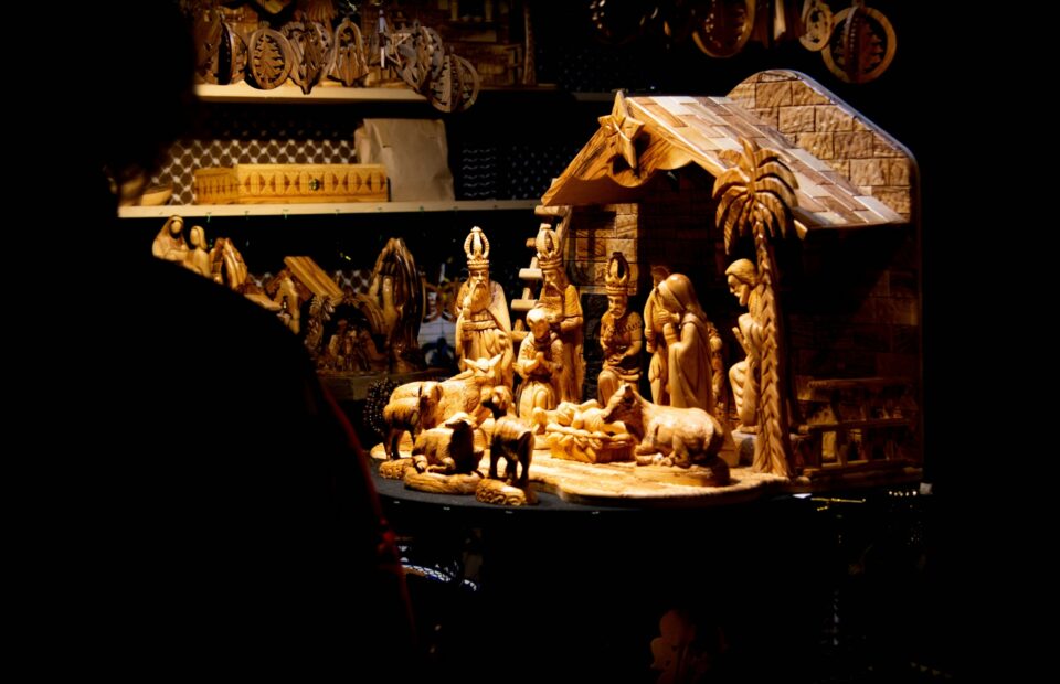 A wooden nativity scene with figurines of the Holy Family, Mary, Joseph, and animals, illuminated and displayed on a table at a craft store.