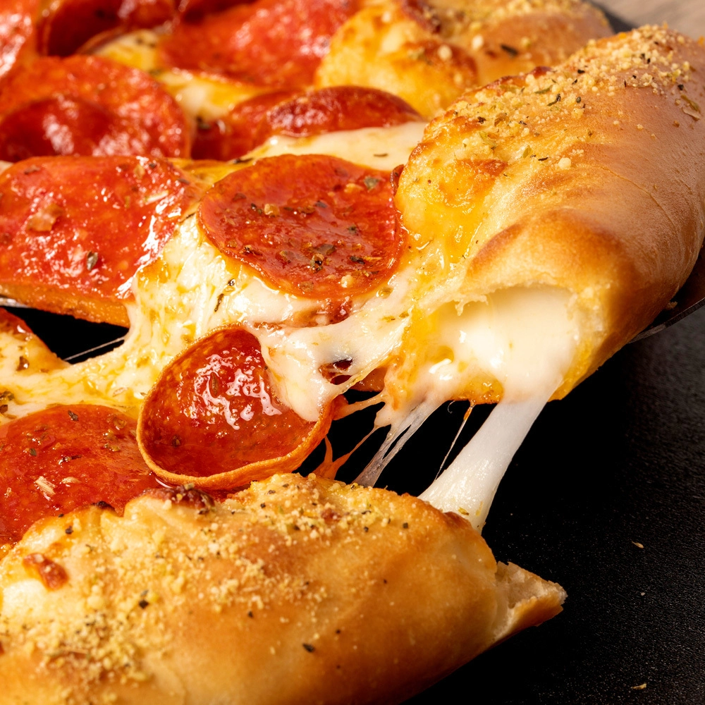 Cheesy pepperoni pizza with a crunchy garlic bread stick, topped with seasonings, against a black background.